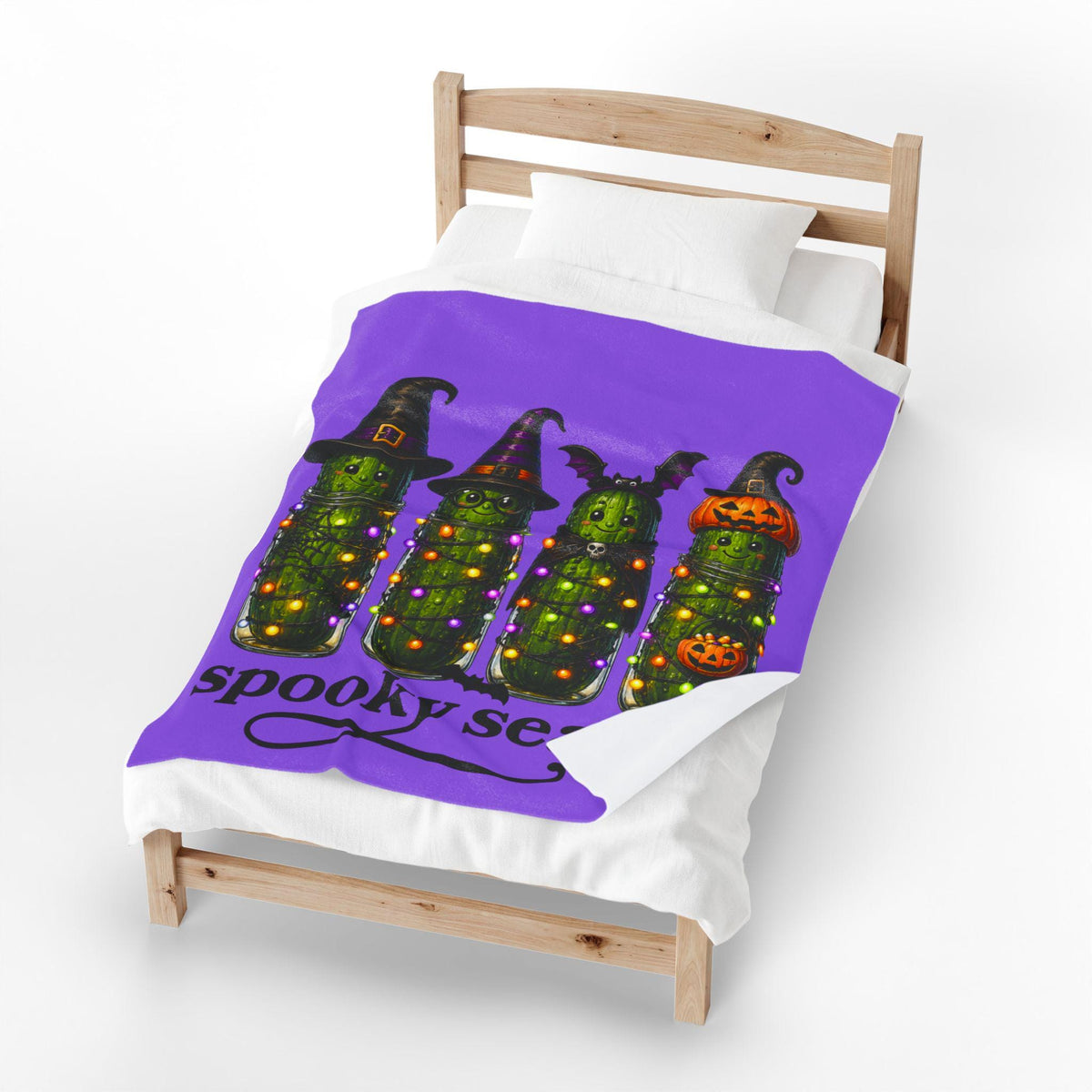 Purple Halloween blanket on a bed featuring four playful pickle characters in witch hats and pumpkin costumes with glowing lights and spooky season lettering