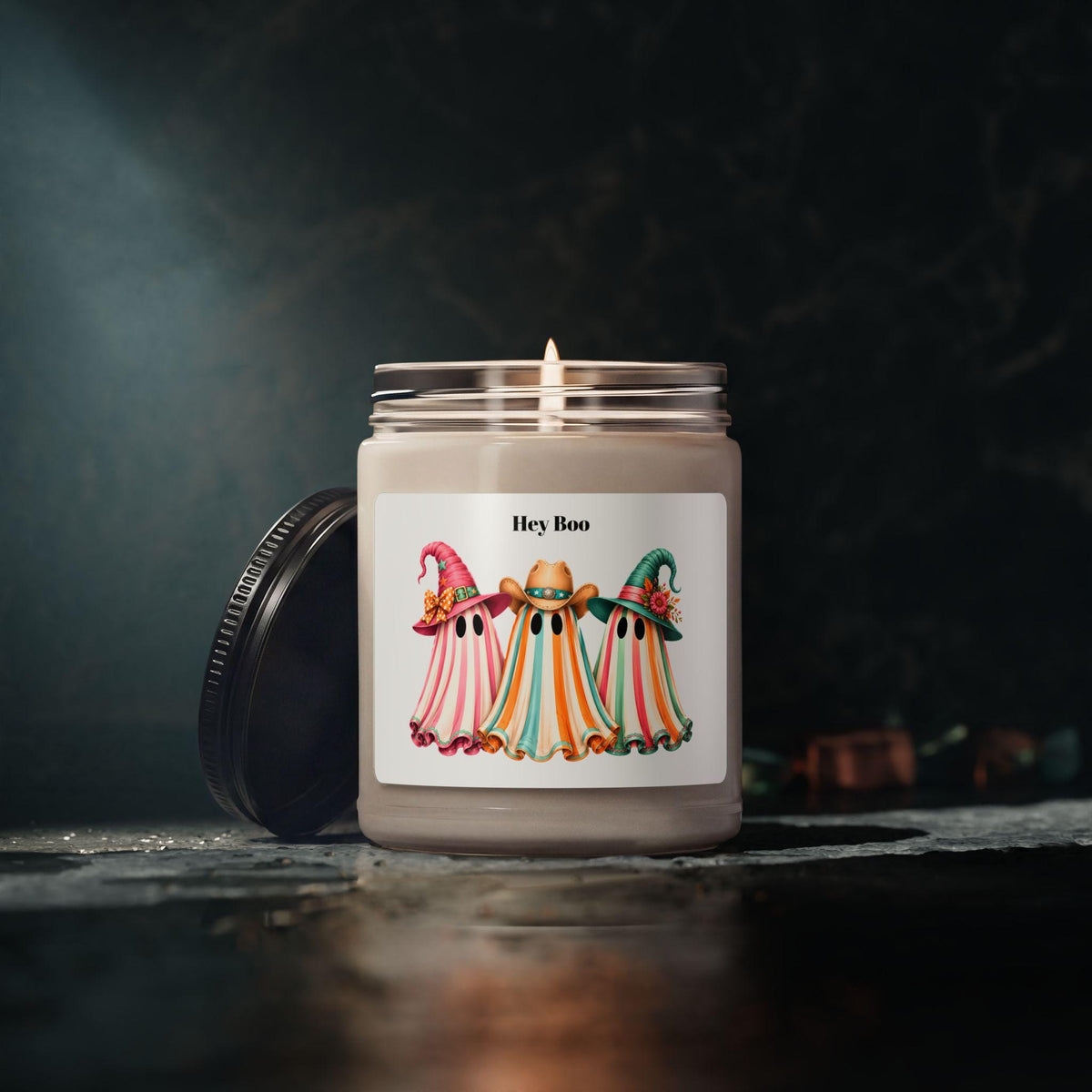 Glass soy candle with three colorful ghost figures wearing cowboy hats on a Hey Boo label and a warm flame for seasonal home decor