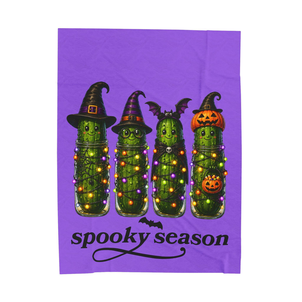 Purple Halloween blanket with four whimsical pickles wearing witch hats pumpkin helmets and bat wings above spooky season lettering from Drizzle and Tizzle