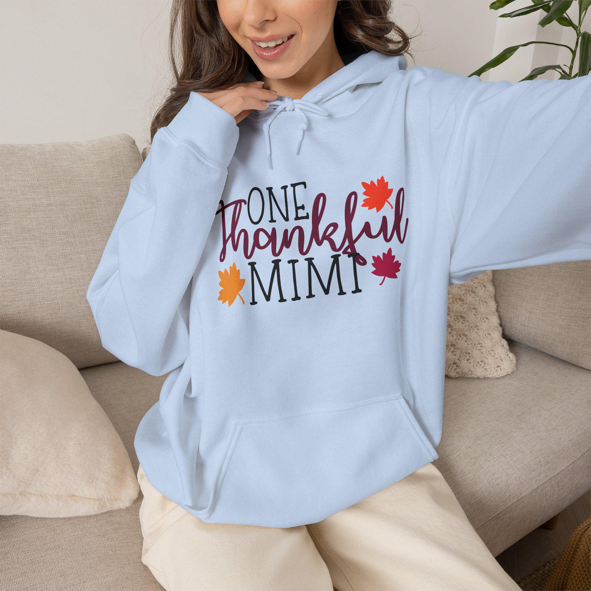 Woman wearing a light blue graphic hoodie reading One Thankful Mimi with colorful autumn leaves styled as cozy seasonal womens fashion