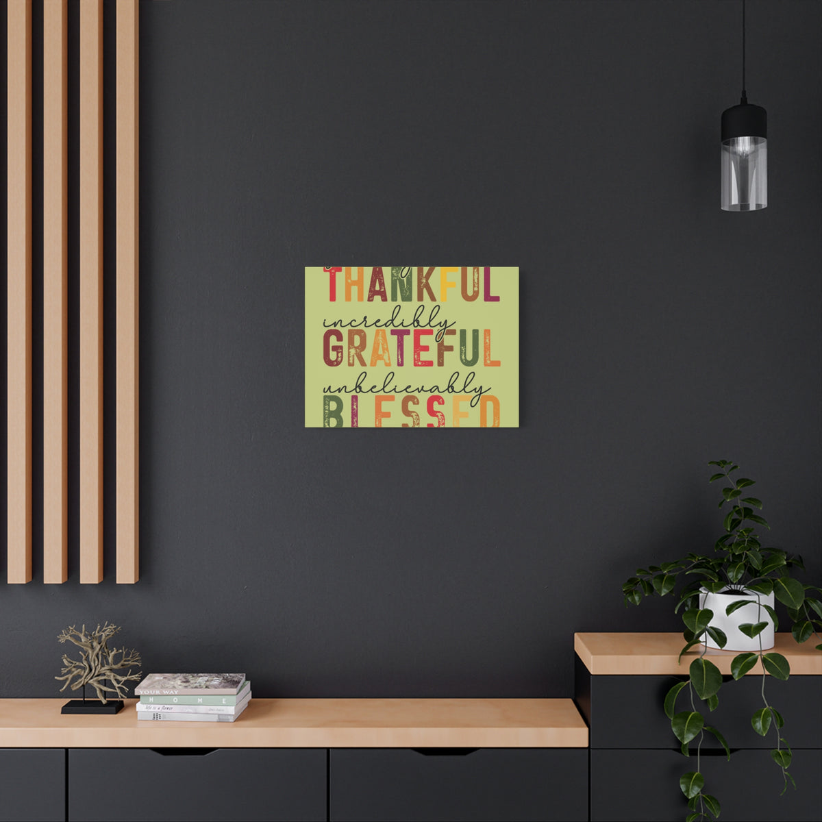 Autumn canvas wall art reading THANKFUL incredibly GRATEFUL unbelievably BLESSED above a wood console in a dark modern home with a hanging light and plant