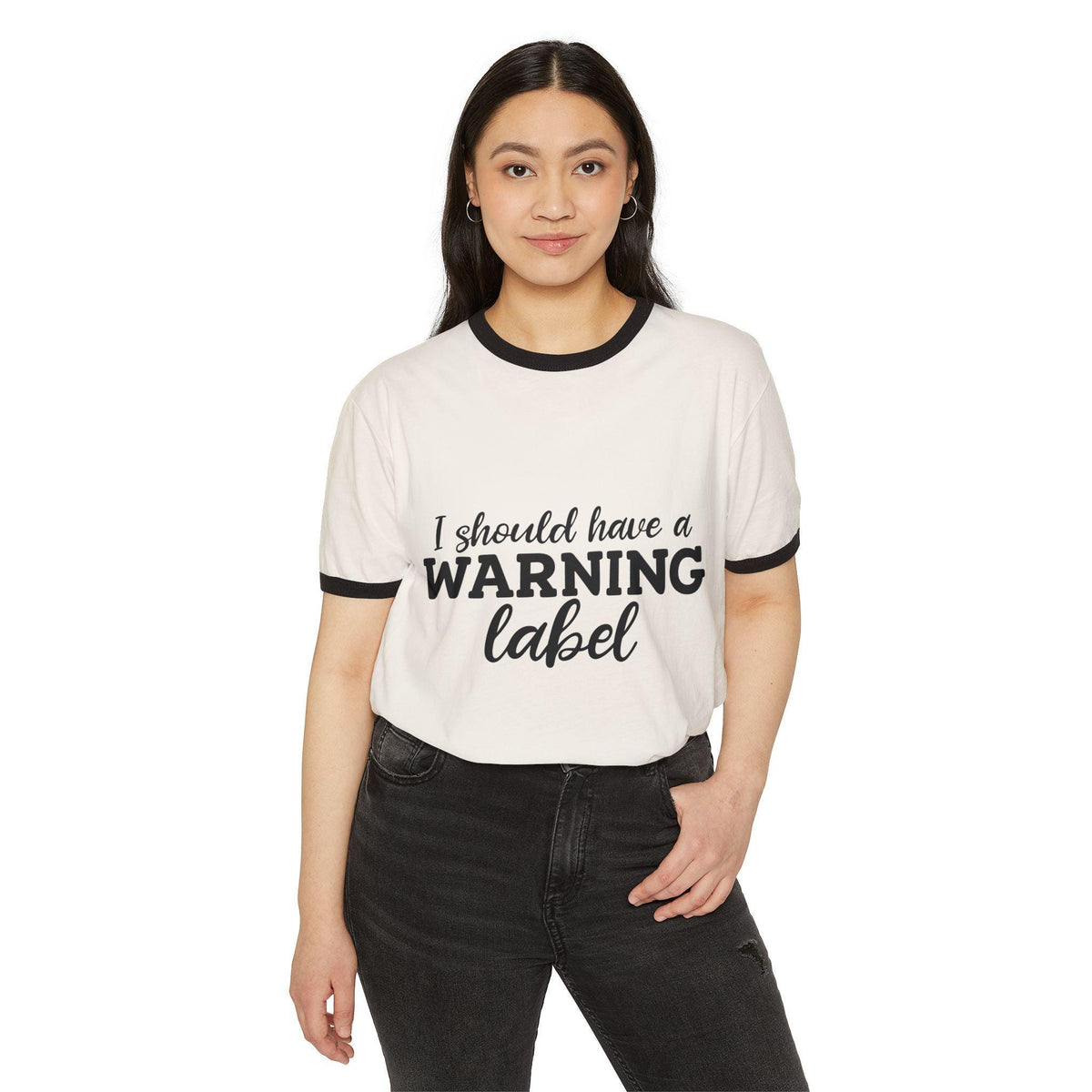 Woman modeling a cream ringer tee with black trim and playful I Should Have a Warning Label text paired with dark jeans