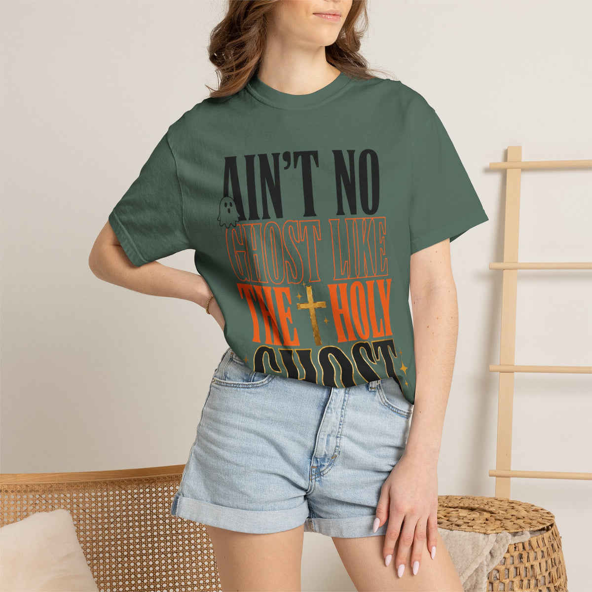 Woman wearing a forest green graphic tee with bold vintage lettering reading Aint No Ghost Like the Holy Ghost styled with light denim shorts