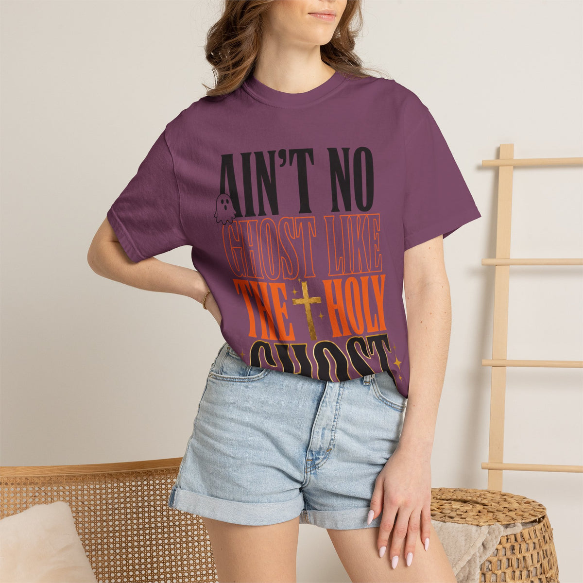 Woman wearing a purple Ain’t No Ghost Like the Holy Ghost graphic tee with light denim shorts in a relaxed indoor setting