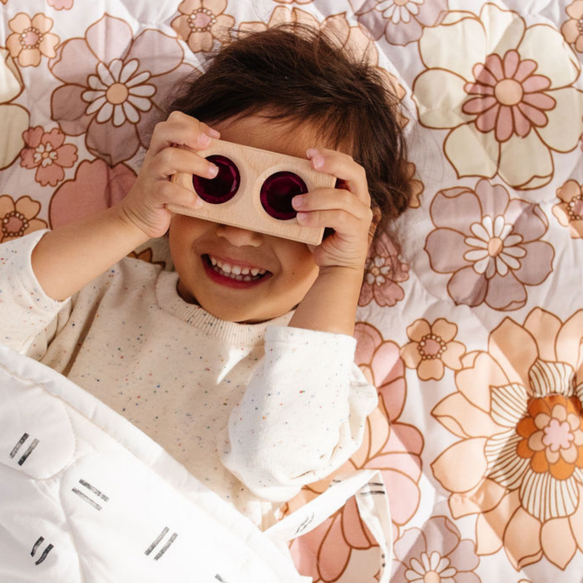 Child smiling while holding a cardboard viewer on a soft floral quilted picnic blanket from DC-Toki Mats in the Home & beyond collection