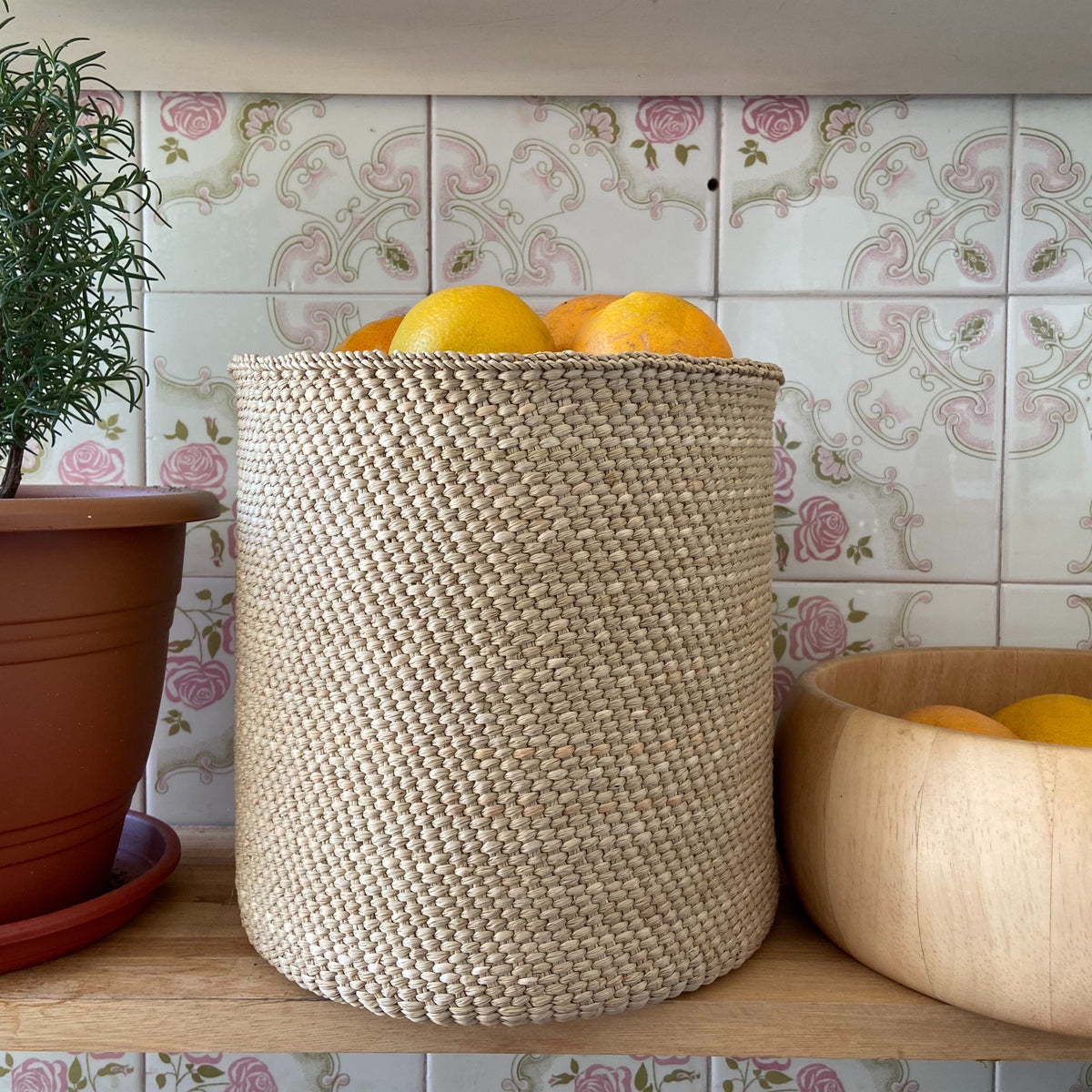 Natural woven fiber basket filled with oranges on a kitchen counter beside a wooden bowl and potted plant from DC Powered by People for Home and beyond