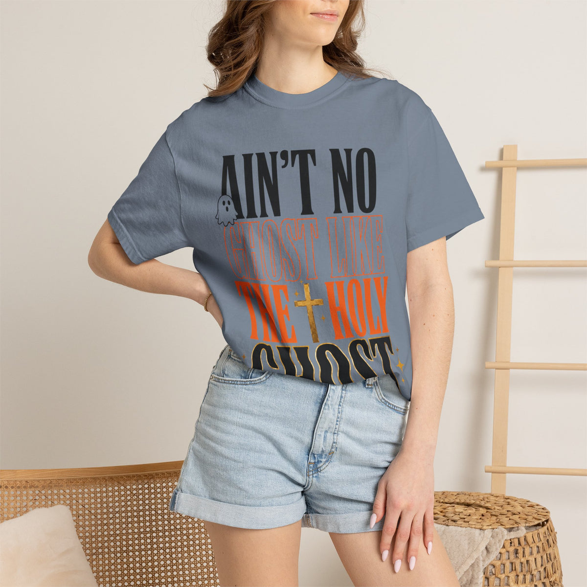 Woman wearing a faded blue graphic T shirt with bold black and orange text reading Ain't No Ghost Like the Holy Ghost styled with denim shorts