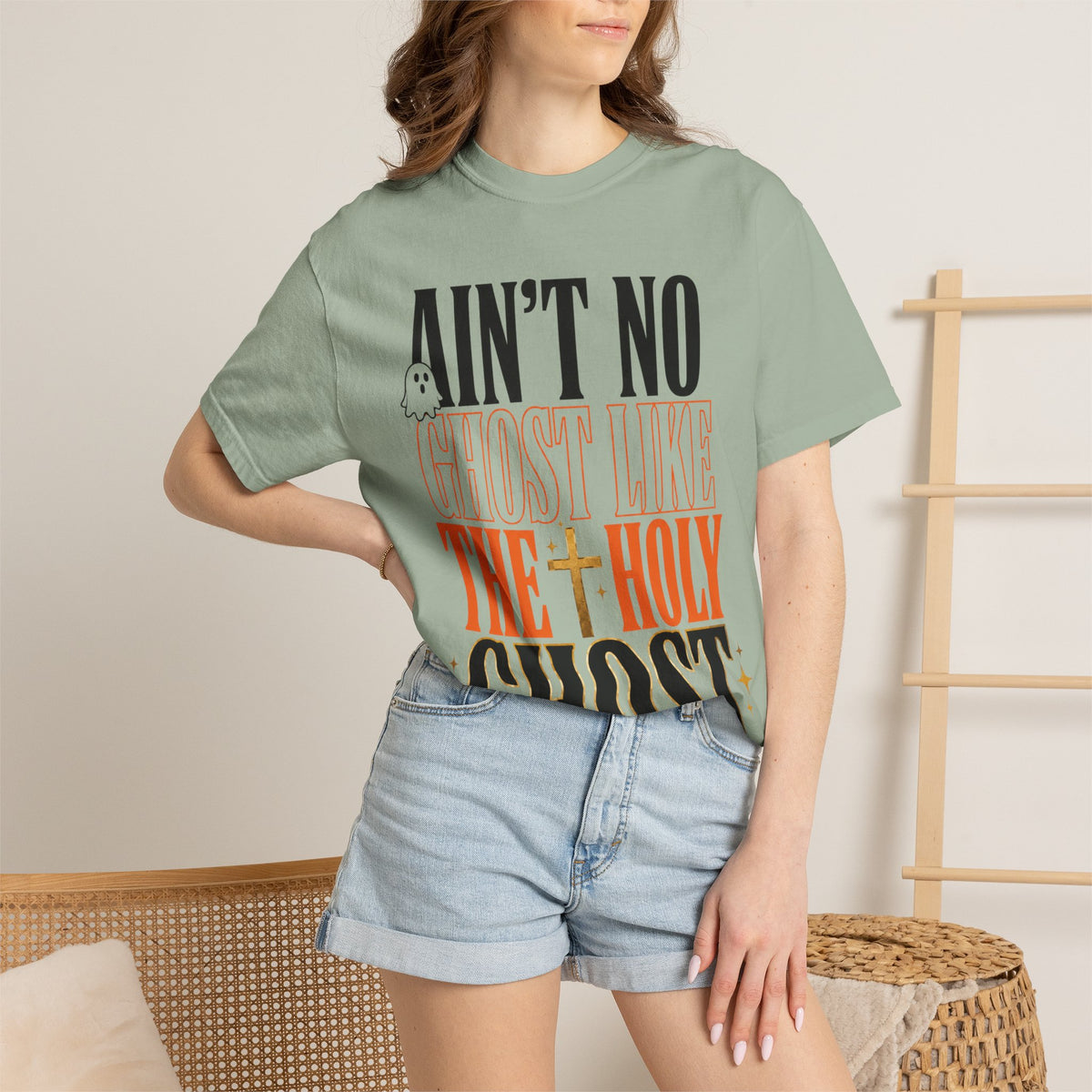 Woman wearing a sage green graphic tee with Aint No Ghost Like the Holy Ghost lettering styled with denim shorts for a casual summer fashion look