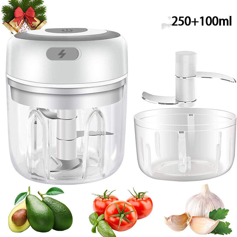 Mini electric food chopper with transparent bowl and stainless steel blade, shown with garlic, tomatoes, avocado, and herbs.
