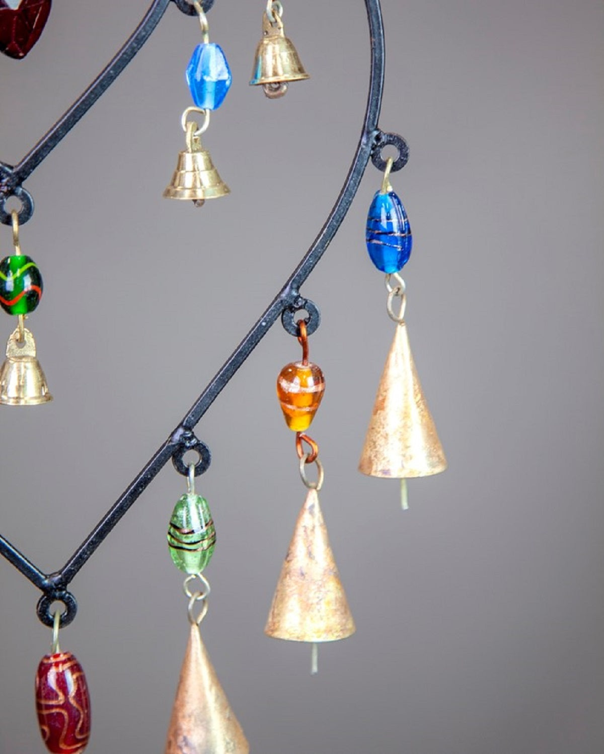Decorative hanging chime with colorful glass beads brass bells and cone shaped metal chimes on a curved black frame for home decor