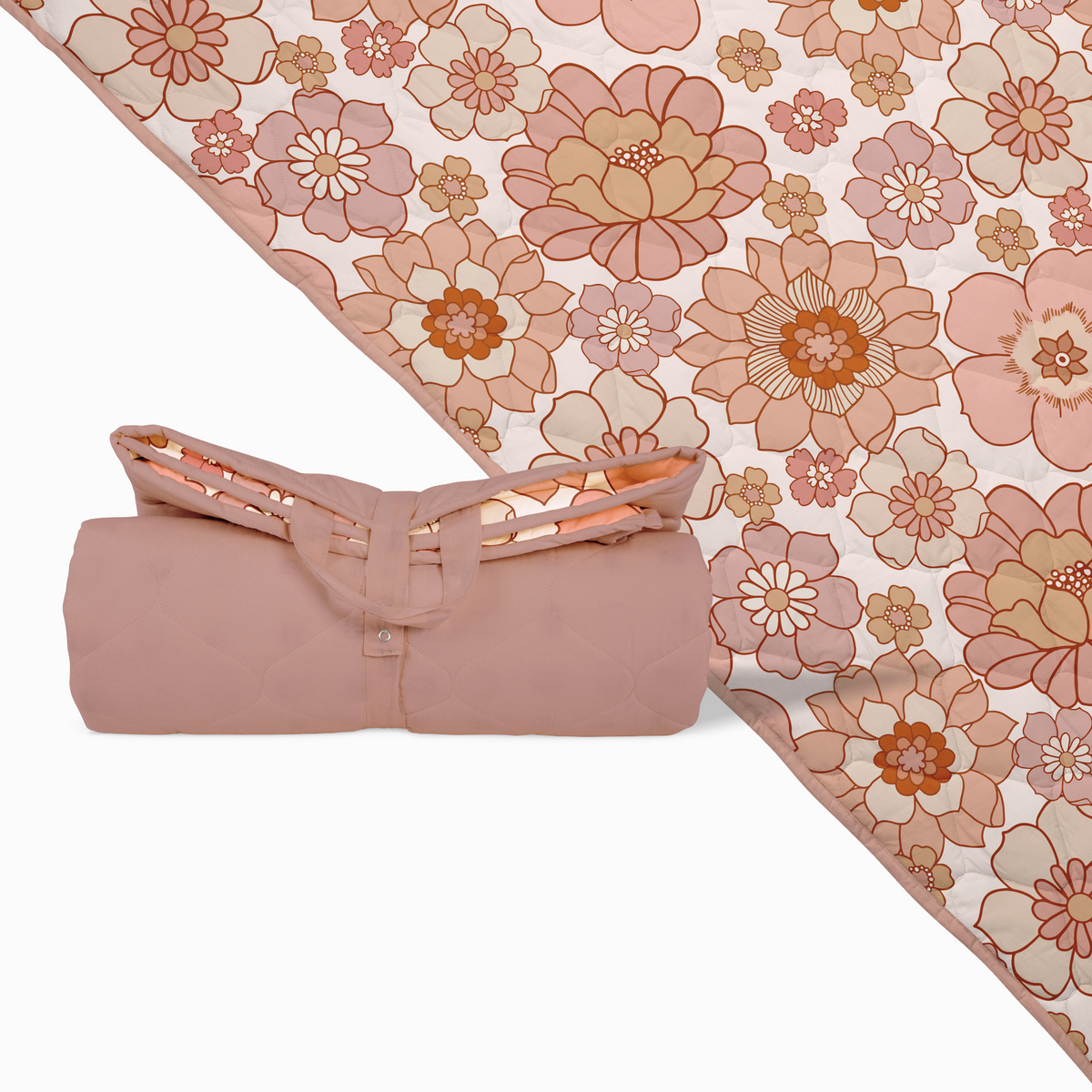 Rolled floral quilted picnic blanket in soft blush and terracotta tones with a convenient carry handle shown beside the unfolded blanket