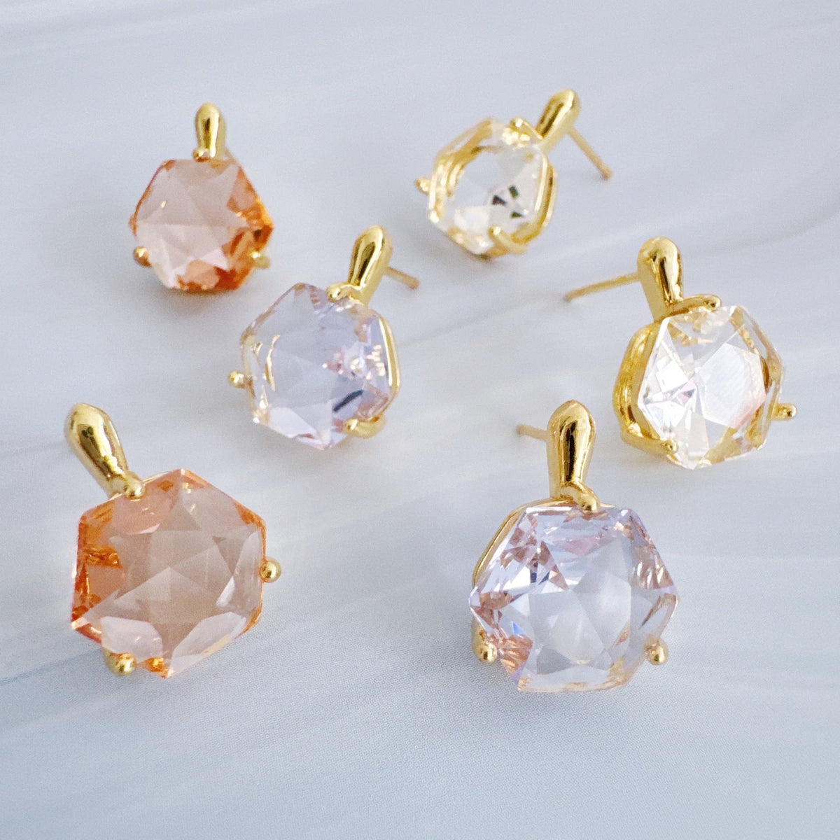 Five faceted gemstone drop earrings in sculpted gold settings arranged on a pale surface from Ellison + Young Jewelry for women's fashion and gifts