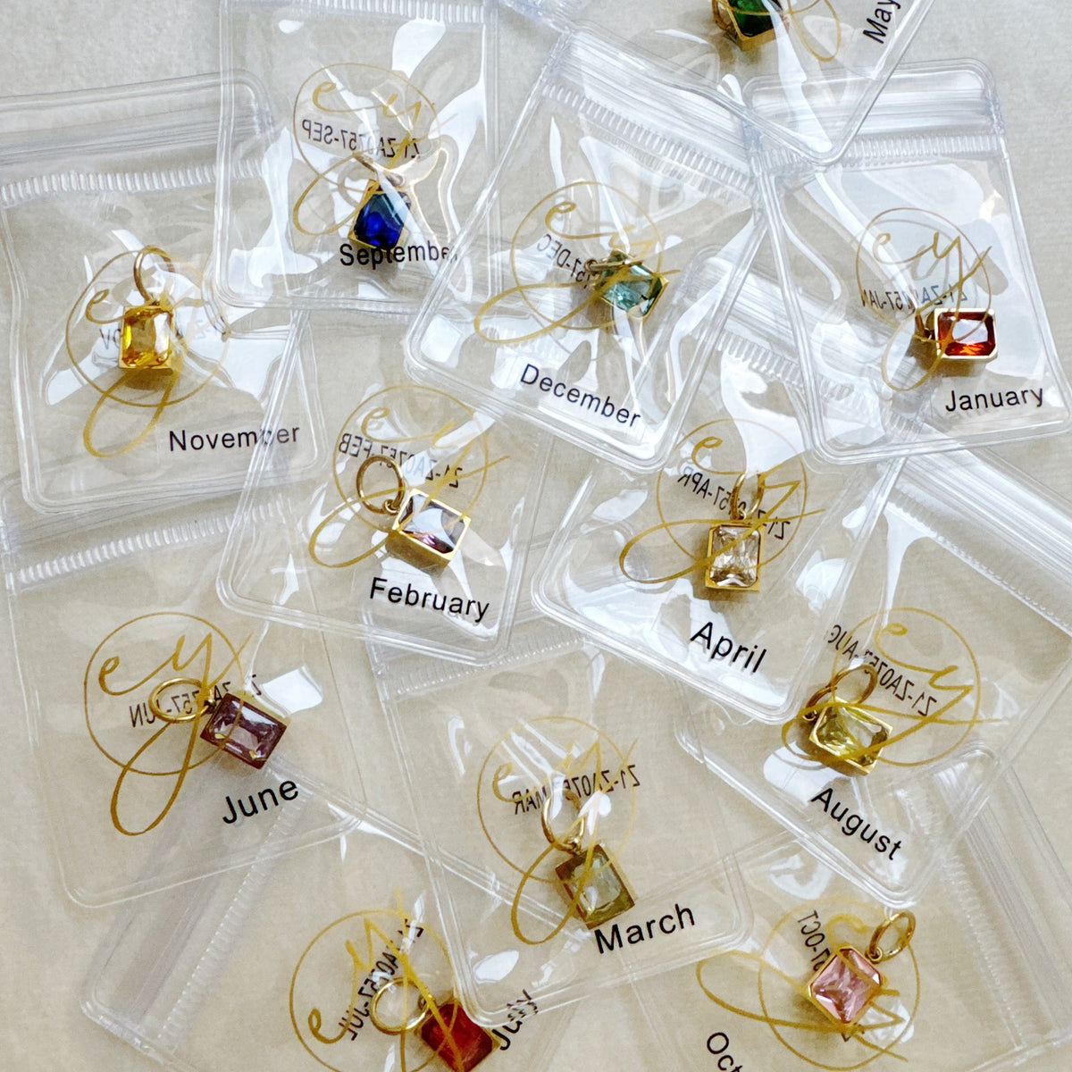 Gold tone birthstone charm pendants in clear pouches labeled by month for stylish women's jewelry from Ellison and Young