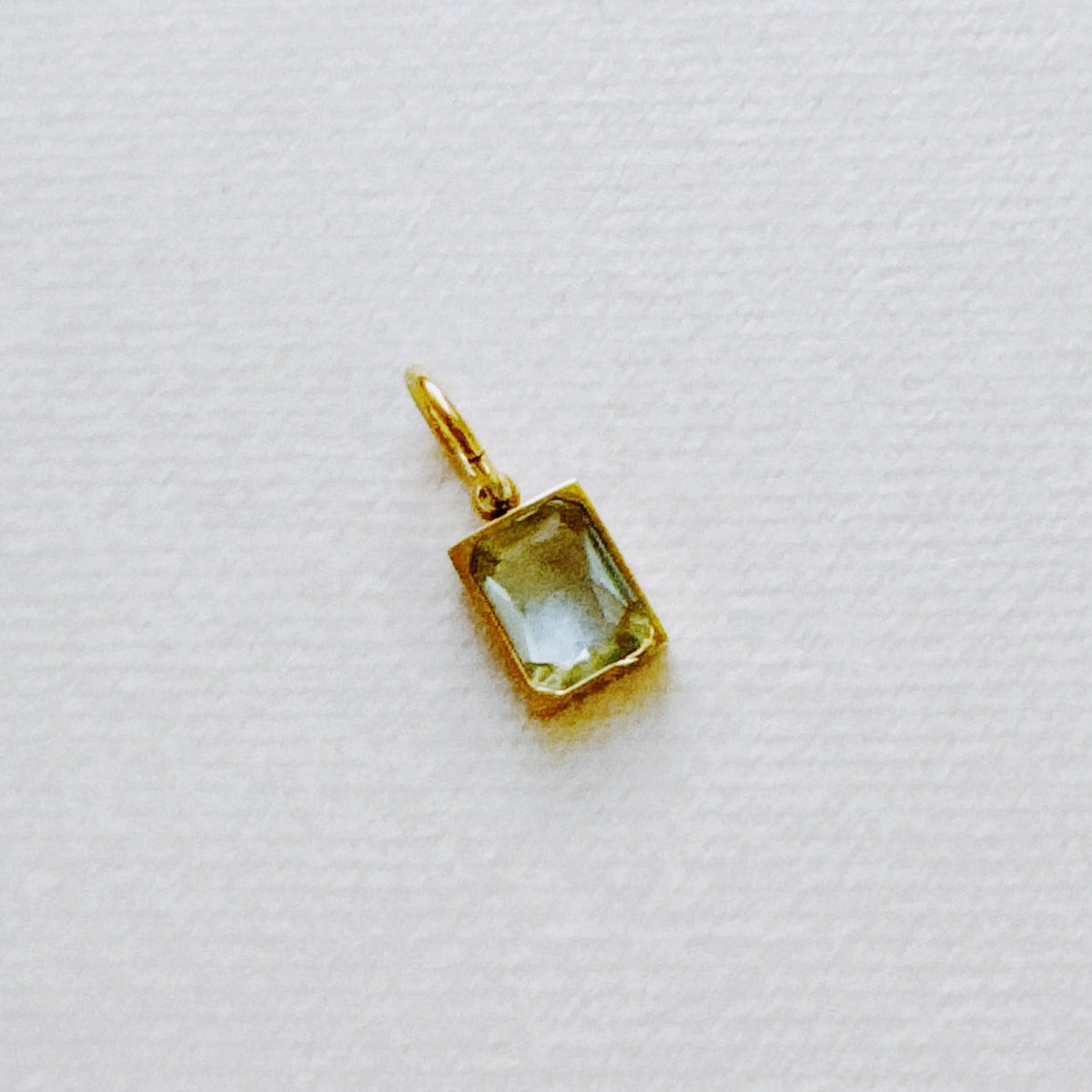 Gold rectangular birthstone pendant with a pale faceted gemstone on textured white fabric from Ellison and Young for women's jewelry and gifts for her