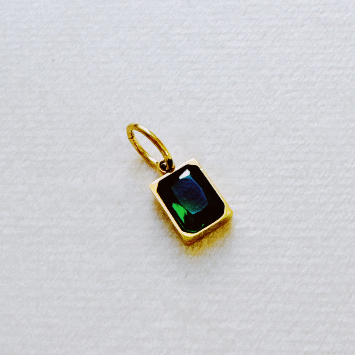 Gold rectangular birthstone pendant featuring a dark blue and green iridescent stone on a white background from Ellison and Young Jewelry Best Sellers