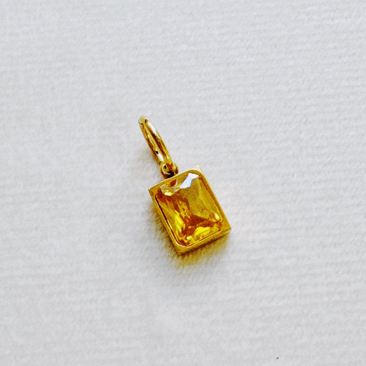 Gold rectangular faceted birthstone pendant from Ellison and Young styled as a charming womens jewelry accessory on white fabric for Best Sellers Jewelry