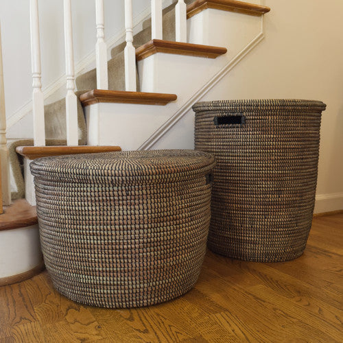 Two handwoven black storage baskets with woven lids sit on a wooden floor beside a staircase adding stylish functional home decor to the space