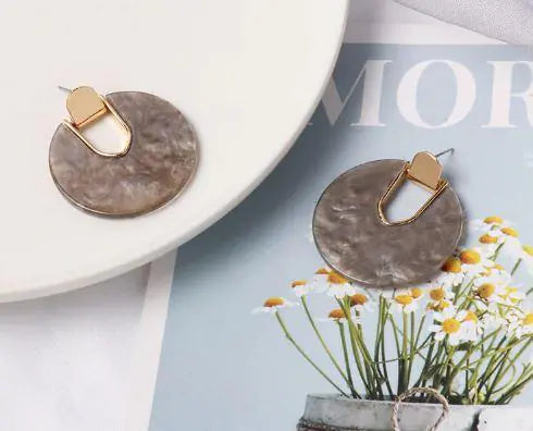 Round marbled drop earrings with gold tone geometric accents styled on a magazine and floral tabletop scene from Drizzle and Tizzle Jewelry