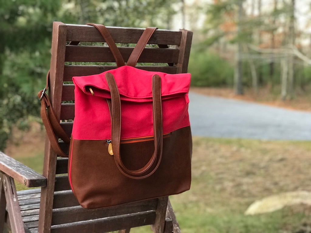 Red and brown convertible backpack tote with adjustable backpack straps and carry handles displayed on a wooden chair outdoors by DC Canopy Verde