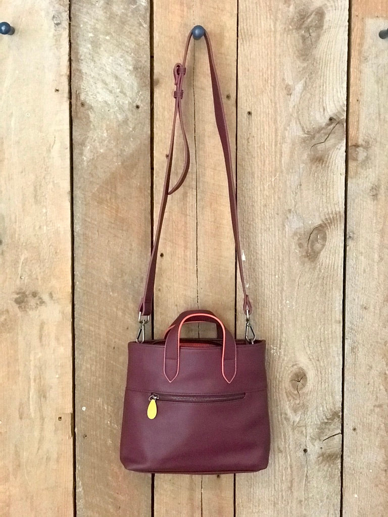 Burgundy womens crossbody satchel with top handles front zip pocket and adjustable strap displayed on rustic wood by DC Canopy Verde from Bags and Belts