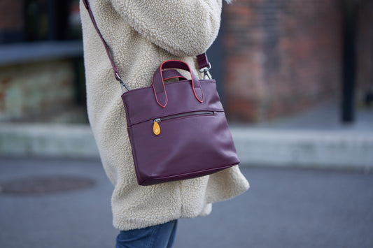 Woman in a cream sherpa coat carrying a plum purple crossbody satchel with top handles and gold hardware from DC-Canopy Verde in Bags and Belts