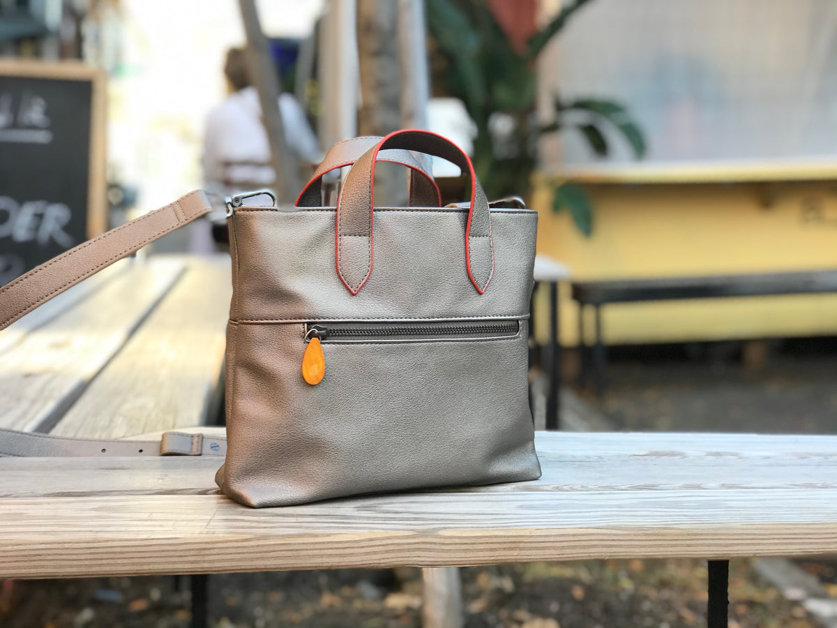 Taupe gray crossbody satchel with red stitched handles and adjustable strap plus front zip pocket on a wooden table by DC-Canopy Verde in Bags and Belts