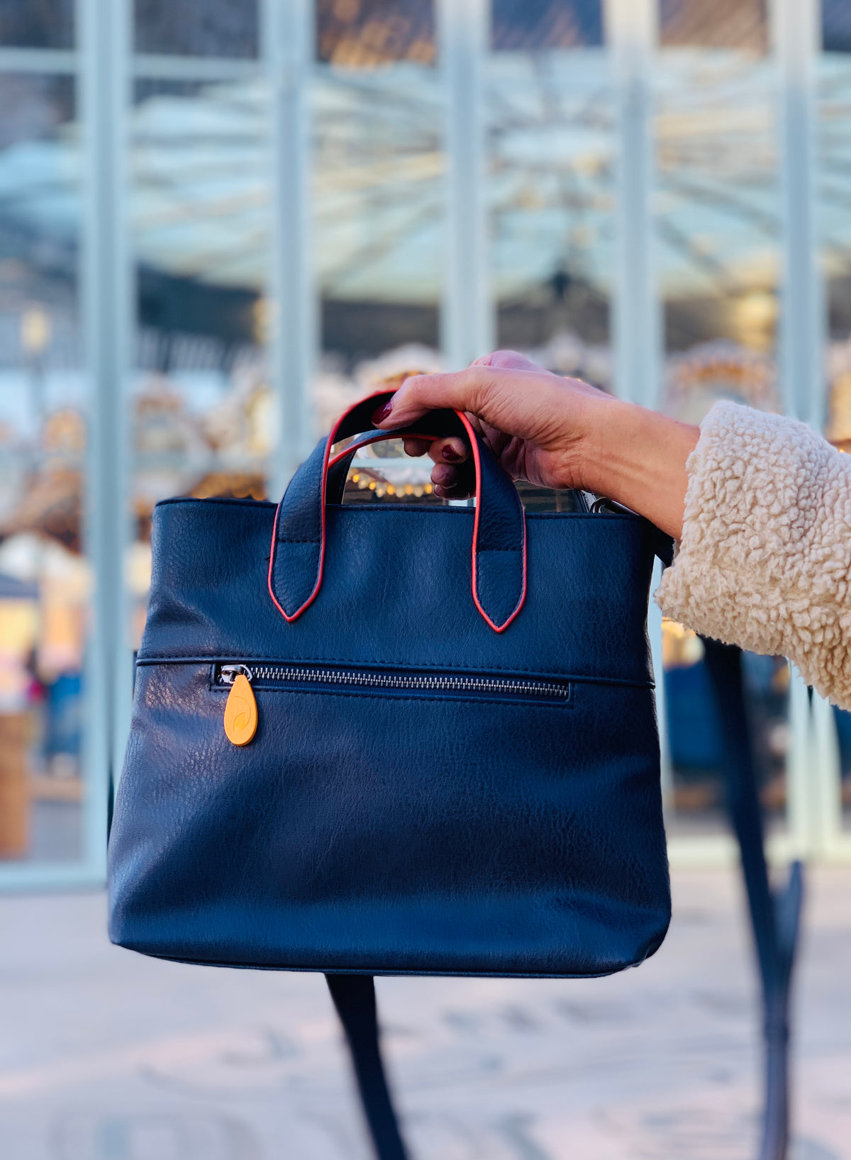 Navy blue womens crossbody satchel with red trim top handles and front zip pocket held outdoors by DC Canopy Verde from Bags and Belts collection