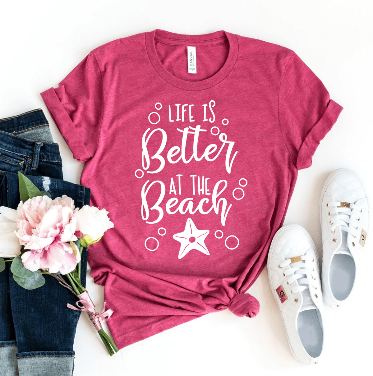 Burgundy unisex graphic tee reading Life Is Better At The Beach with a starfish design styled with jeans flowers and white sneakers for womens fashion