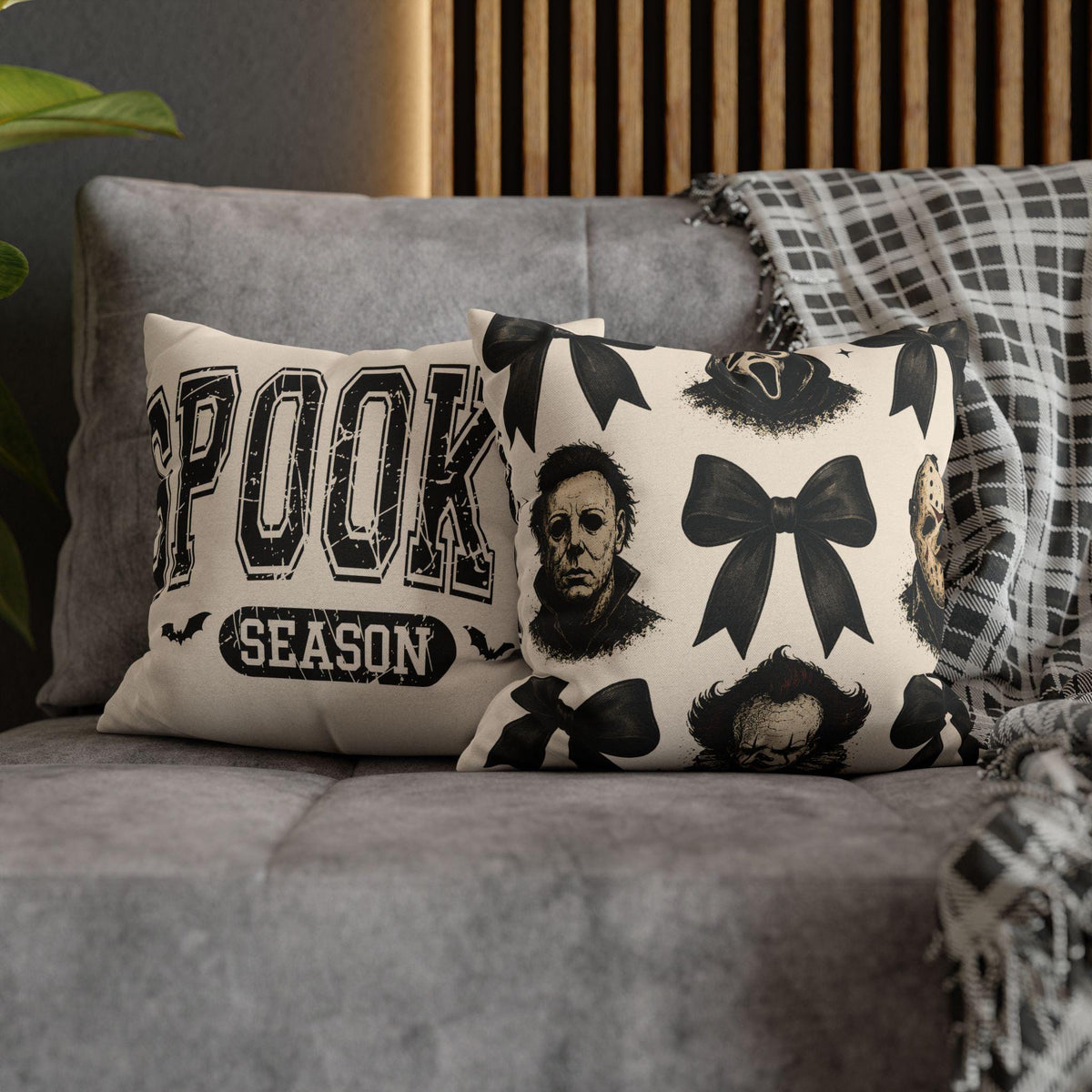 Cream square pillowcase with black horror masks and bow motifs styled on a gray sofa beside a plaid throw for seasonal home decor