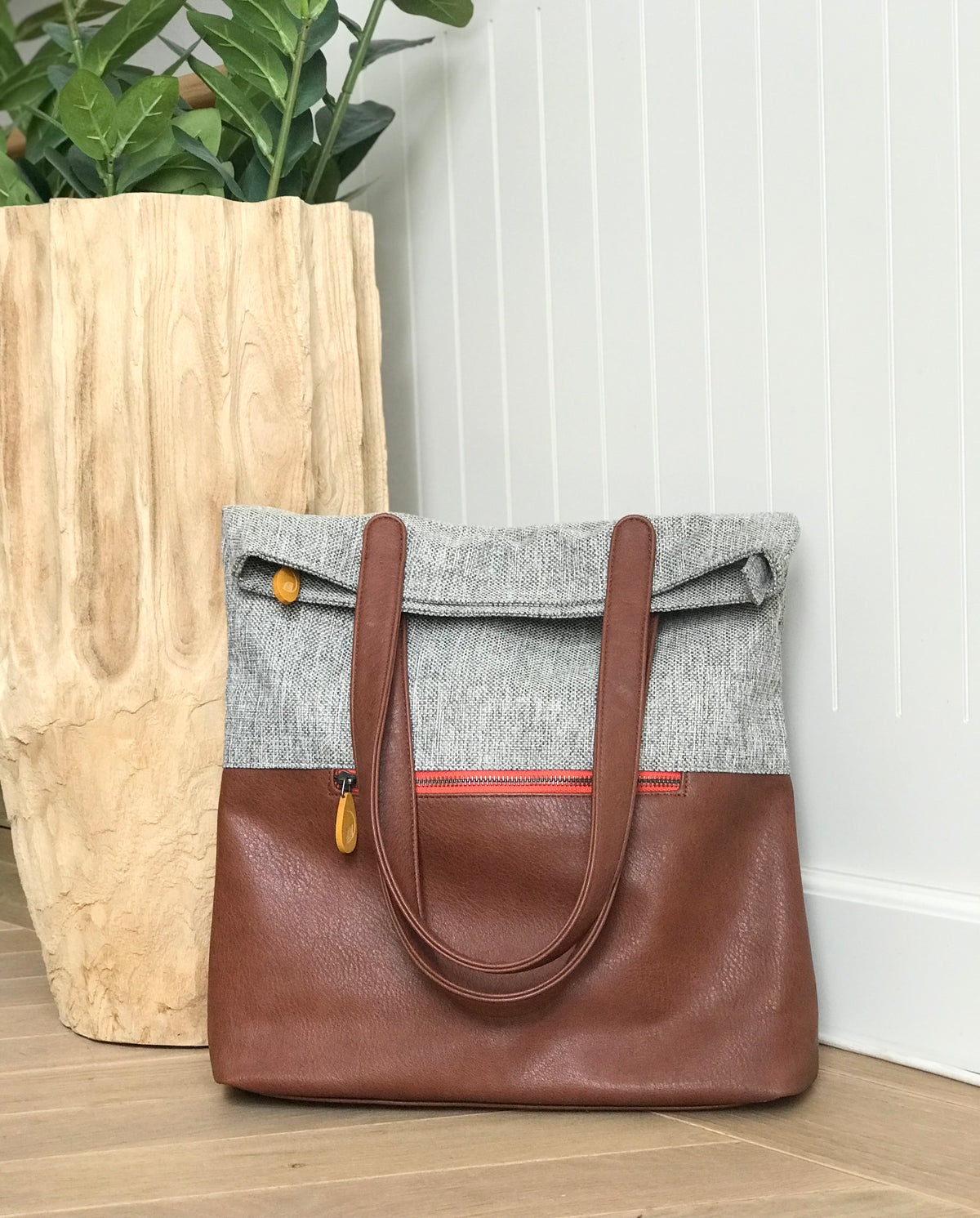 Gray and brown convertible backpack tote with long shoulder straps and front zipper displayed beside a plant from DC-Canopy Verde Bags and Belts collection