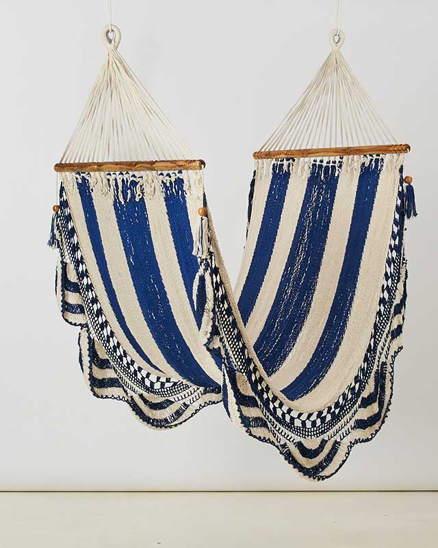 Two handmade cotton hammocks in blue and cream stripes hang from wooden bars with decorative fringe for a comfortable home retreat and relaxed bohemian style