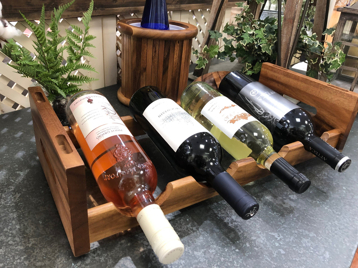 Wooden stackable wine rack holding four wine bottles on a tabletop surrounded by greenery from DC Kalmar Home in Home and beyond