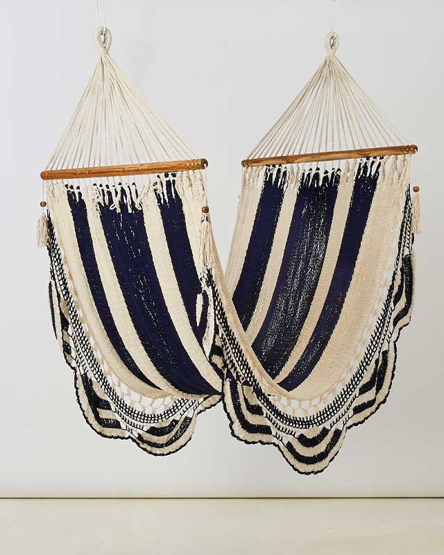 Two cream and navy striped cotton hammocks hang side by side from wooden spreader bars against a light wall for a cozy home decor accent